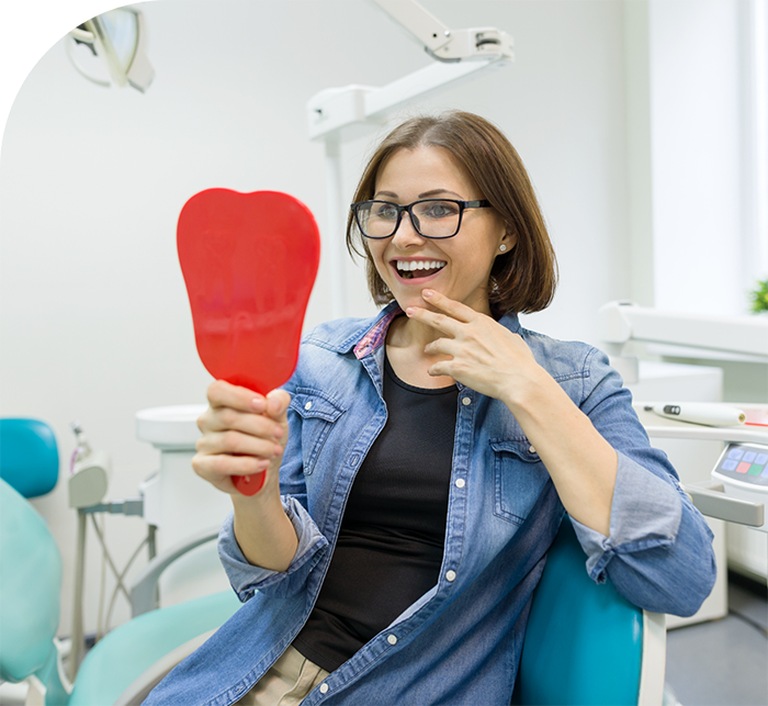 Woman in dental chair looking at her smile in a mirror