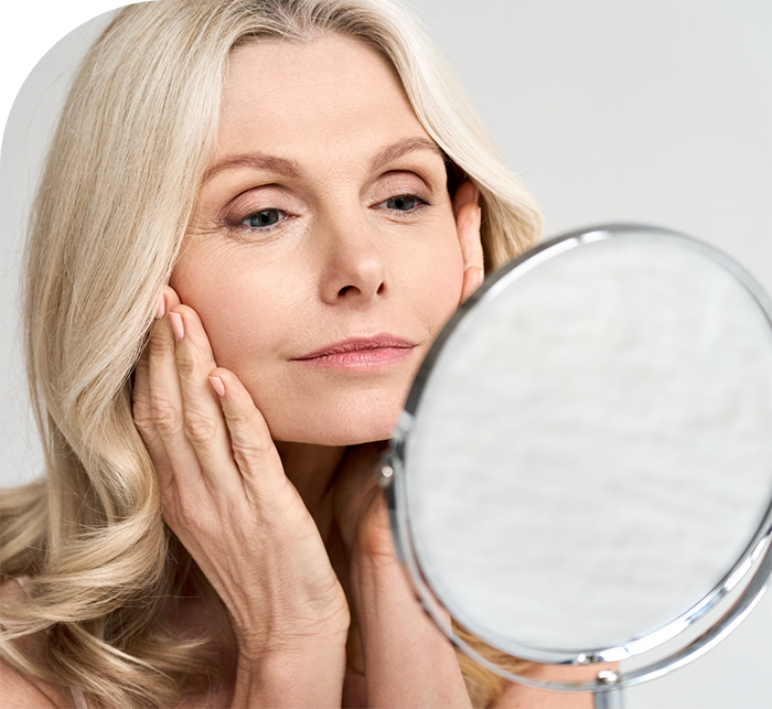 Woman looking at her face in mirror after dermal fillers and injectables in Hanover