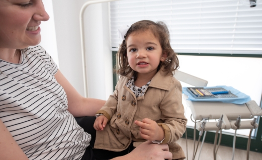 Young girl sitting on her mothers lap in dental chair