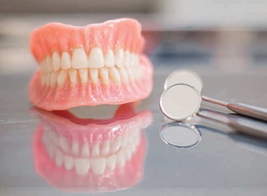 Full dentures on desk next to two dental mirrors