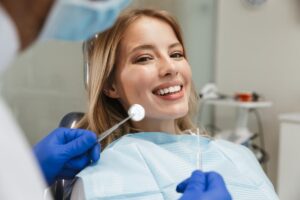 a woman sitting in a dental exam chair smiles after getting porcelain veneers