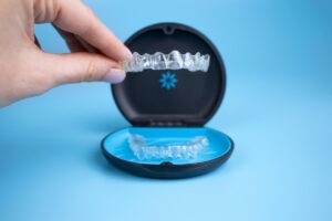 person picks up a clear aligner from its case and talks about the cost of invisalign
